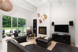 Een moderne woonkamer met een grote televisie, comfortabele zitplaatsen, een open haard en uitzicht op het landschap.