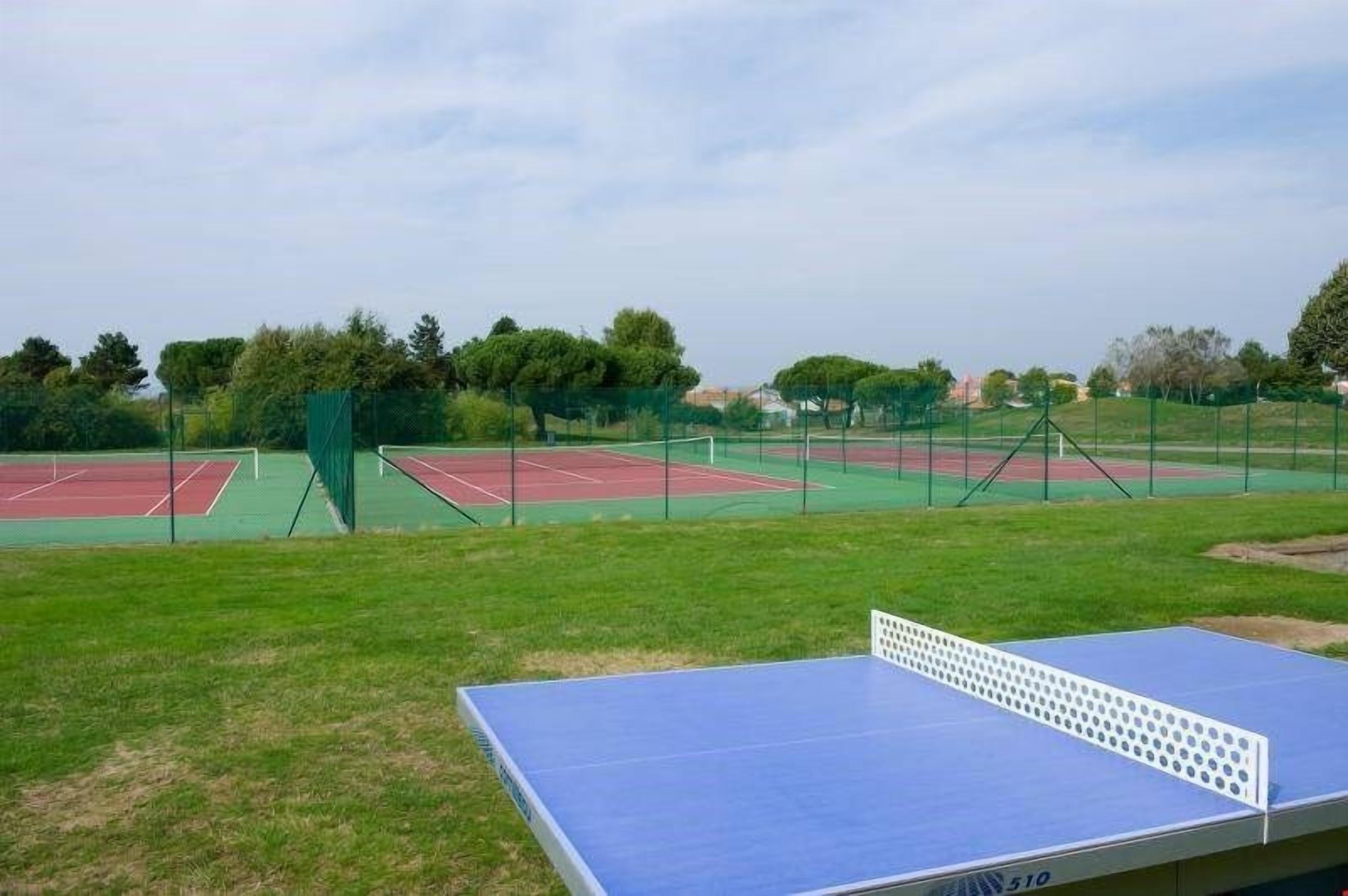 A tennis court with a blue table tennis table in the foreground.