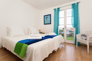 Une chambre d’hôtel avec deux lits, un balcon offrant une vue agréable et un fauteuil en osier.