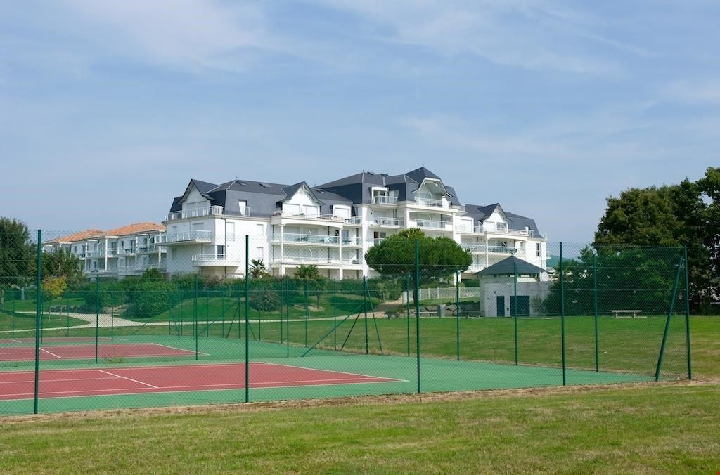 A multi-story residential building with a tennis court in the foreground.