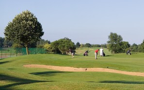 Un parcours de golf avec un bunker de sable, des arbres et des joueurs.