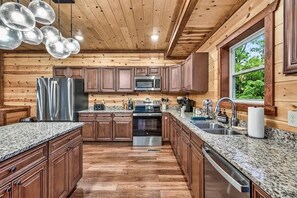 Eine moderne Küche mit Holzschränken, Granit Arbeitsplatten, Edelstahlgeräten und einem großen Fenster mit Blick auf Grünflächen.