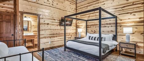 Una cama con dosel en una habitación tipo cabaña de madera, con ventilador de techo, mesita de noche y lámpara.