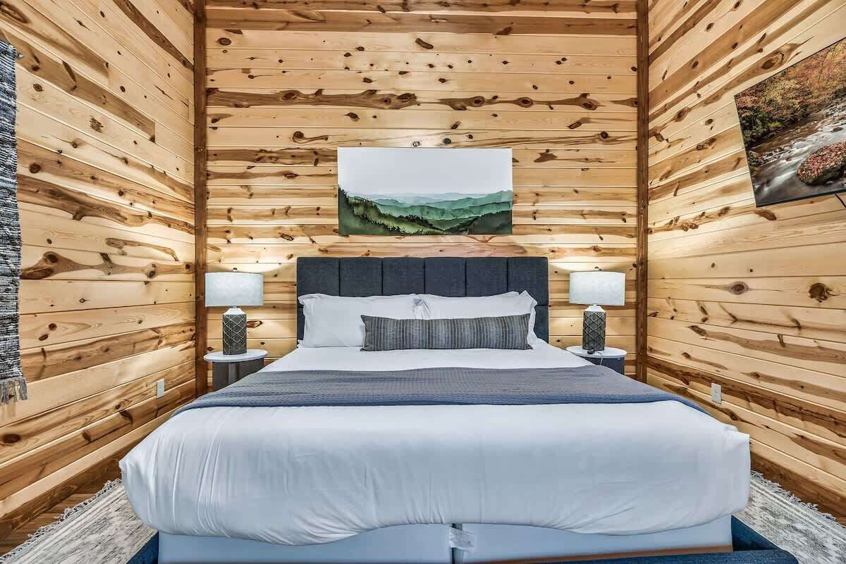 Een slaapkamer in een houten chalet met een bed, twee bedlampen en een schilderij aan de muur.