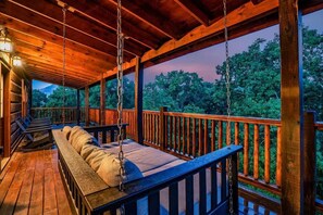 Eine Holzterrasse mit einer Schaukel, Bänken und Blick auf Bäume.
