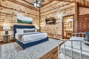 Ein Schlafzimmer einer Holzhütte mit einem Bett, einem Nachttisch, einem Sessel und einem Deckenventilator.