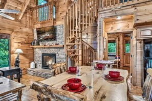 Ein rustikales Holzinterieur mit Kamin aus Stein, einem Esstisch mit roten Schüsseln und einer Treppe, die in ein Obergeschoss führt.