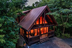 Eine Holzhütte mit geneigtem Dach, großen Fenstern und einer Veranda.