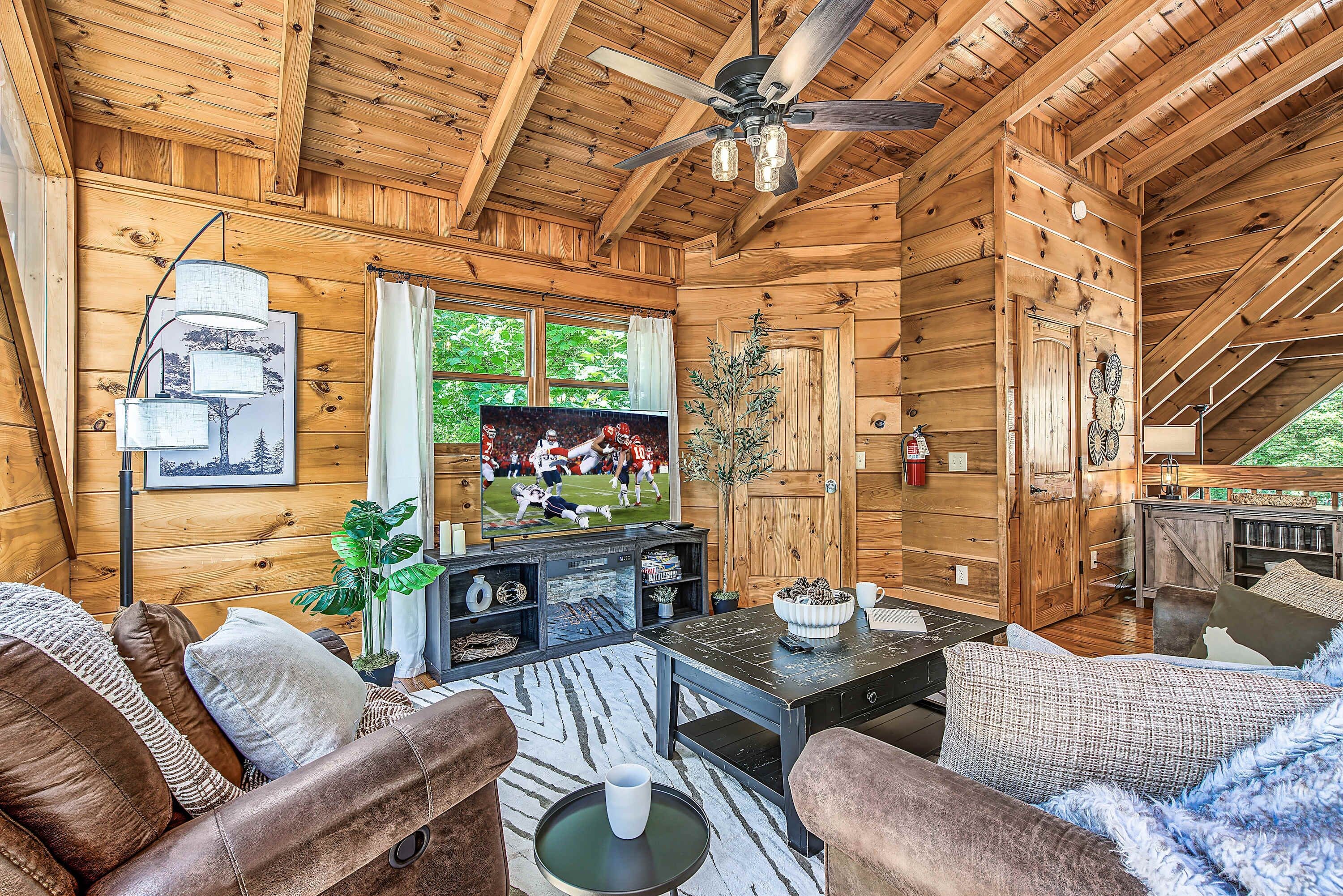 Interior acogedor de una cabaña de madera con ventilador de techo, paredes de madera, televisor y comedor.
