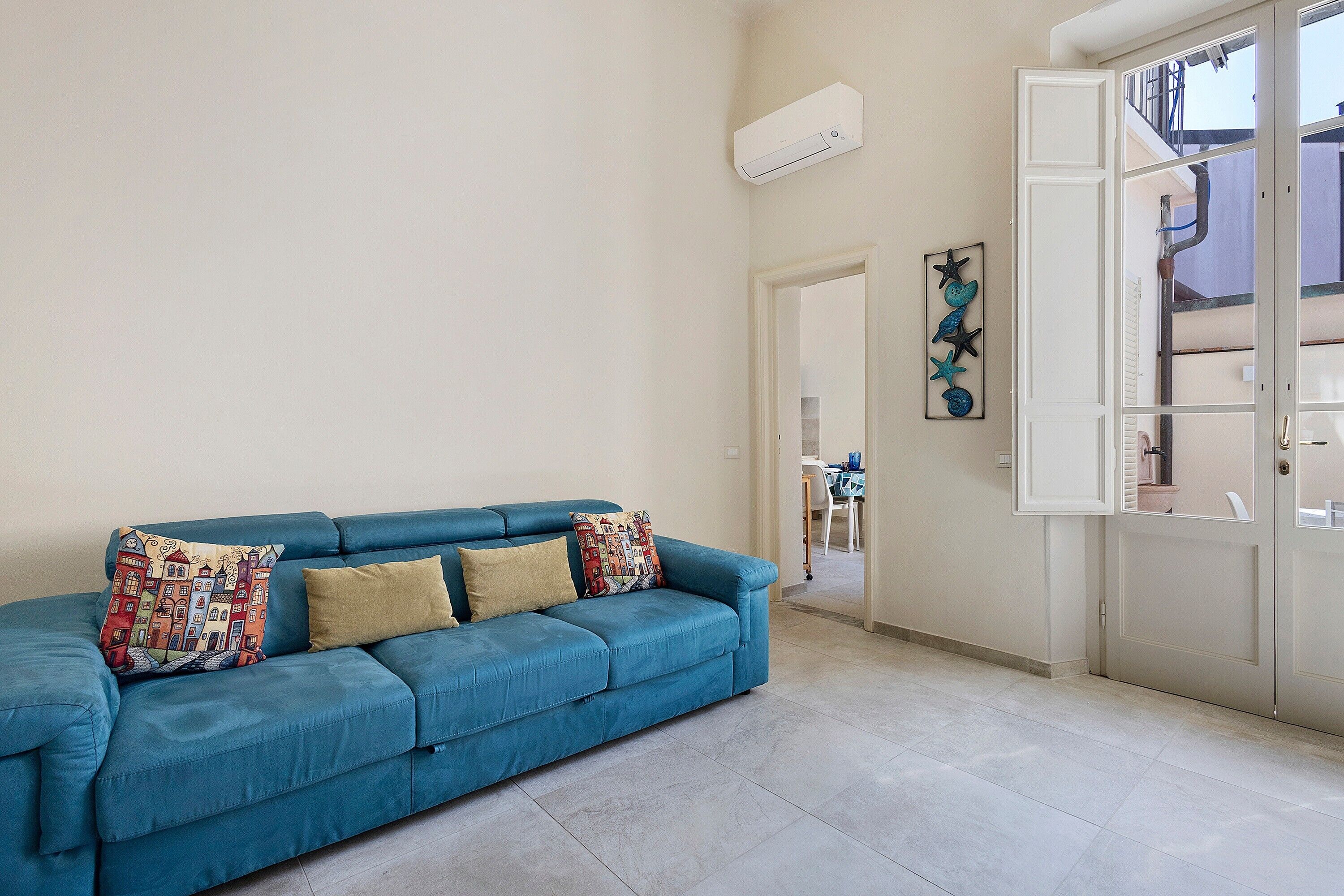 Un divano blu con cuscini decorati in una stanza con pavimento piastrellato e una porta bianca.