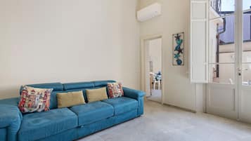 Un divano blu con cuscini decorati in una stanza con pavimento piastrellato e una porta bianca.
