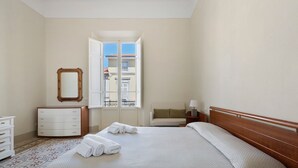 A hotel room with a bed, a dresser, a mirror, and a window with a view of buildings. - Holiday Home 'Villa Lucia' with Sea View, Wi-Fi & Air Conditioning (Viareggio)