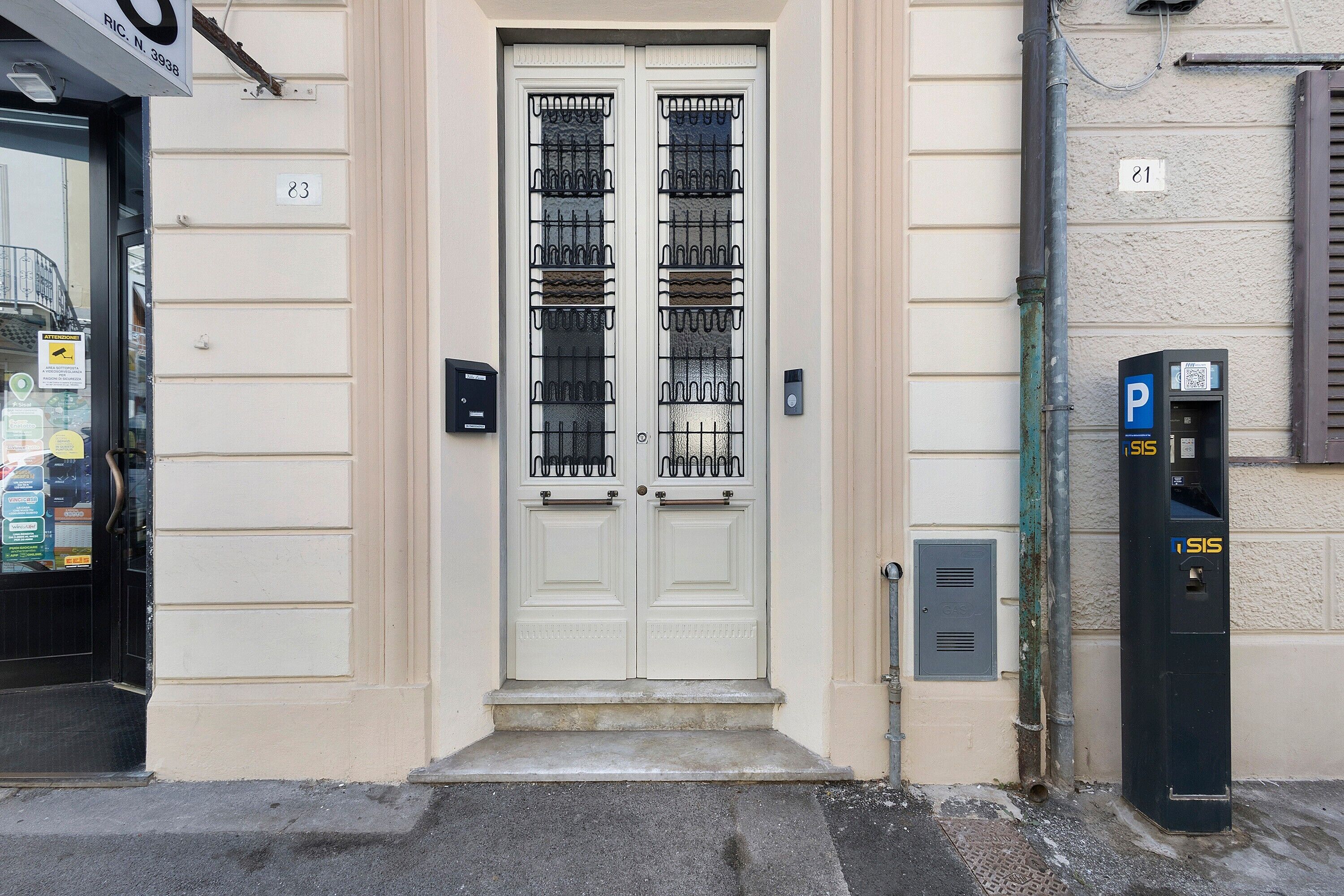 Une porte à deux battants avec un portail en métal, un parcmètre et une boîte aux lettres sur le trottoir.
