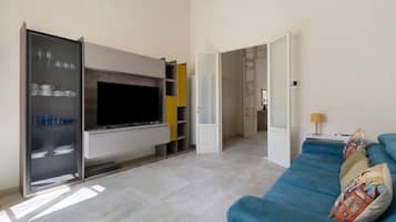 Un soggiorno con una TV a schermo piatto, un divano blu e una vetrina con stoviglie.
