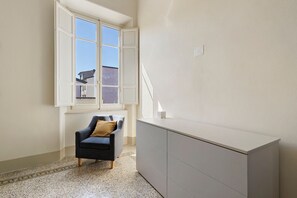 Ein Zimmer mit Stuhl, Schreibtisch und Fenster mit Blick auf Gebäude.