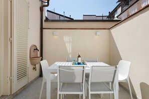 Eine Terrasse mit Tisch und Stühlen, einem wandmontierten Waschbecken und einem Fenster mit Blick auf Gebäude.