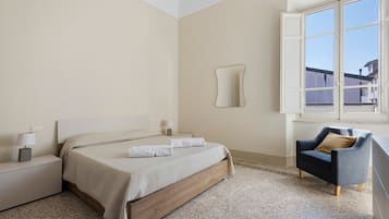 Una camera da letto con un letto, comodini, una sedia, una finestra e uno specchio fissato alla parete.