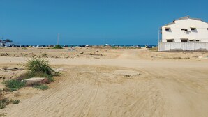 A sandy area with a white building, a dirt road, and a clear blue sky. - A Cozy and Safe 4-Bedroom House, Near the Local Beach. (Salinas)