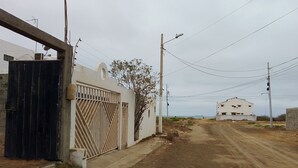 A rural road leading to a white building with a metal gate, surrounded by vegetation and utility poles. - A Cozy and Safe 4-Bedroom House, Near the Local Beach. (Salinas)