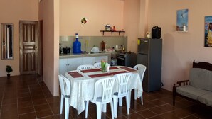 A dining area with a table set for four, a kitchen with a refrigerator and stove, and a sofa in the corner. - A Cozy and Safe 4-Bedroom House, Near the Local Beach. (Salinas)