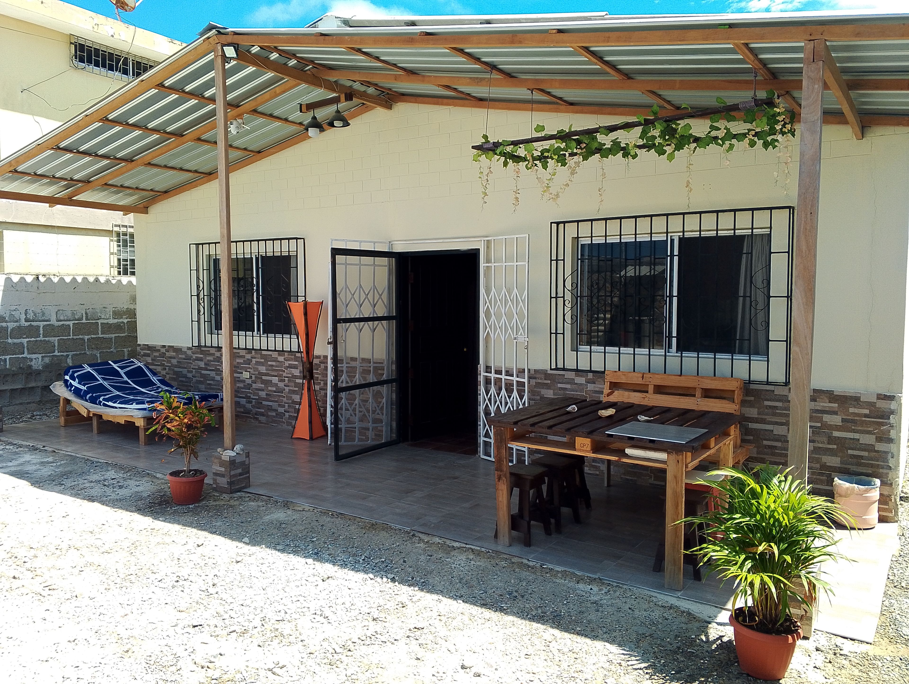 A covered outdoor seating area with a table and chairs, a potted plant, and a bench.