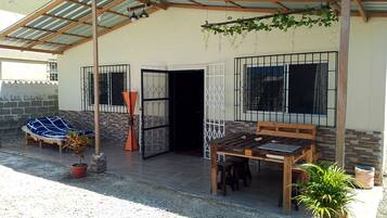A covered outdoor seating area with a table and chairs, a potted plant, and a bench.