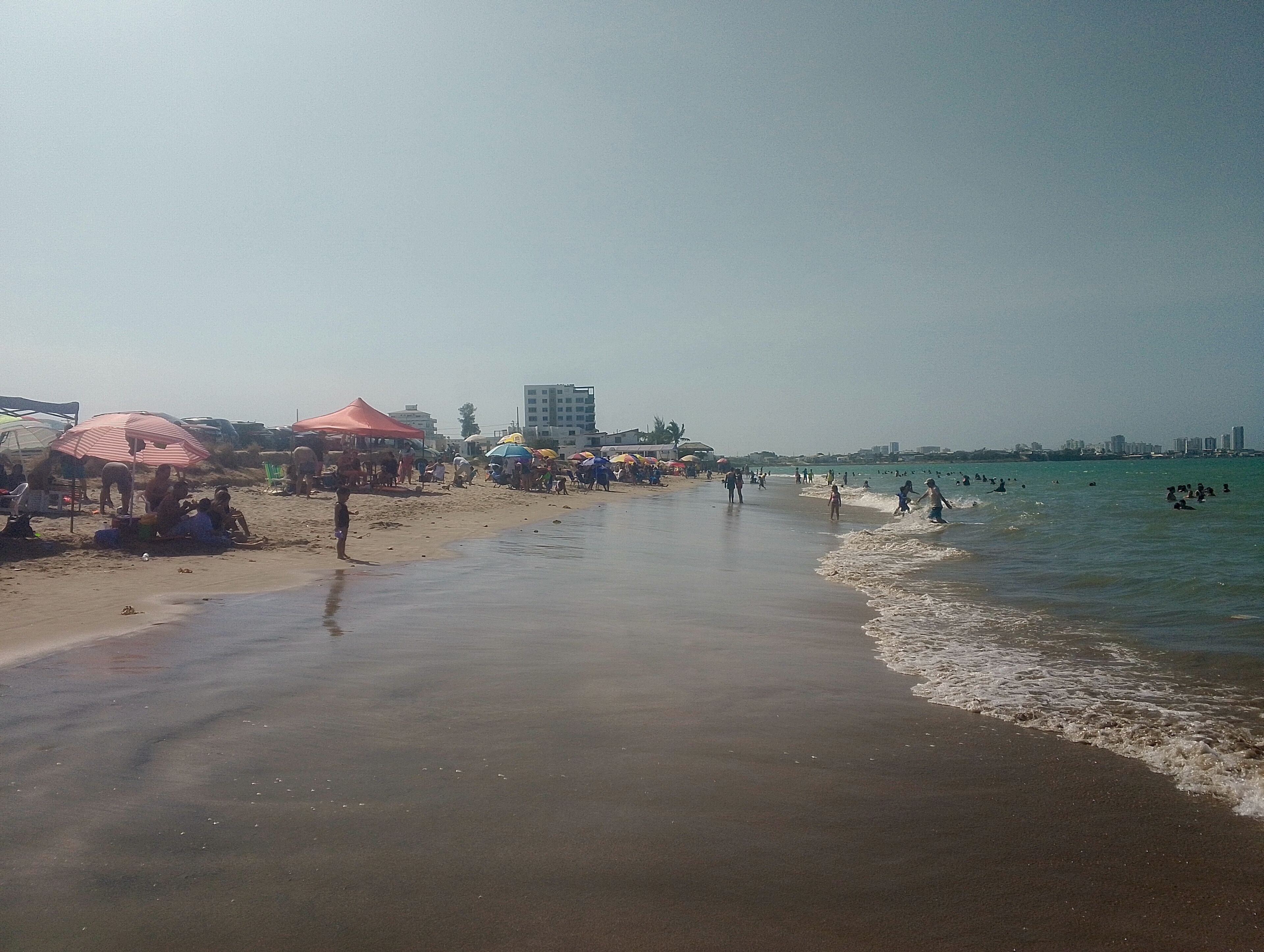 A beach with umbrellas, people, and a building in the background.