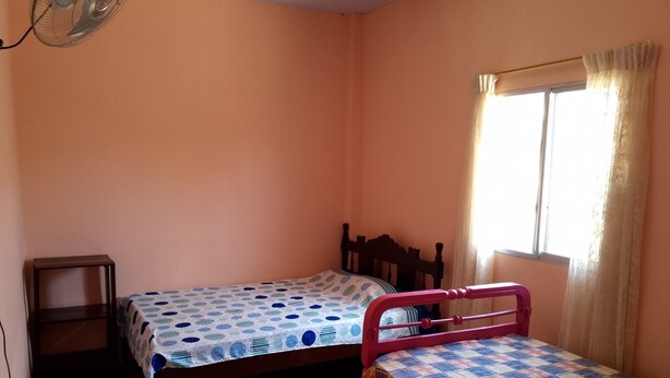 A bedroom with two beds, a window with curtains, and a fan on the wall. - A Cozy and Safe 4-Bedroom House, Near the Local Beach. (Salinas)