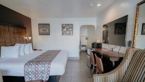 A hotel room with a bed, a desk, a chair, a mirror, and artwork on the walls. - Standard Queen Room (Anaheim)