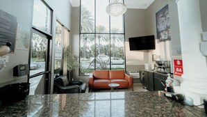 A hotel lobby with a large window, a sofa, a coffee machine, and a television. - Standard Queen Room (Anaheim)