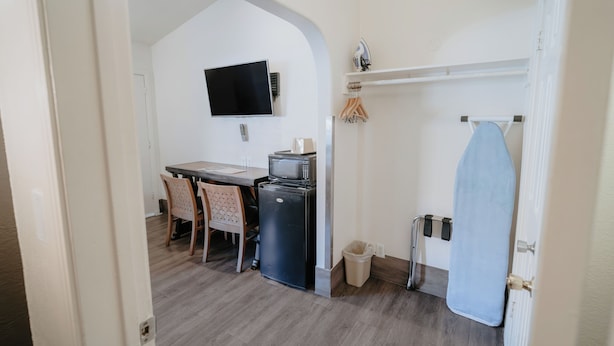 A compact kitchen with a dining area, a TV mounted on the wall, and a small ironing station. - Standard Queen Room (Anaheim)