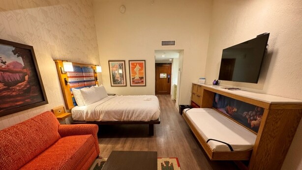 A hotel room with a bed, a sofa, a TV, and a painting on the wall.