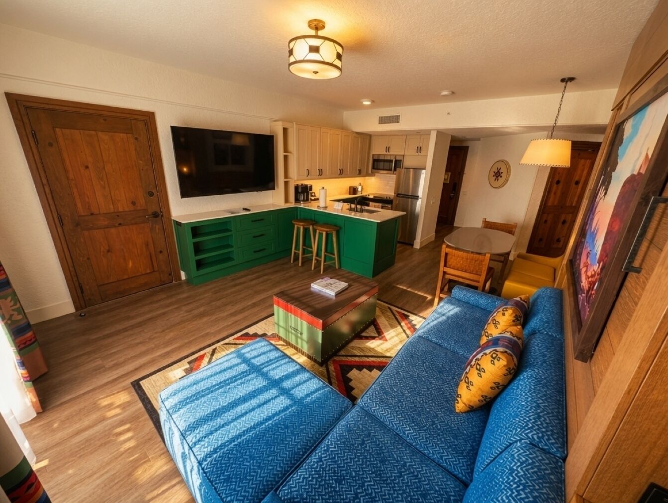 Un ambiente compatto con angolo cottura, un divano con cuscini decorati e una televisione.