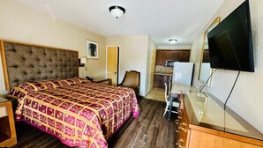 Una habitación de hotel con cama, escritorio, silla, televisión y kitchenette.