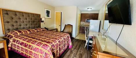 A hotel room with a bed, a desk, a chair, a television, and a kitchenette.