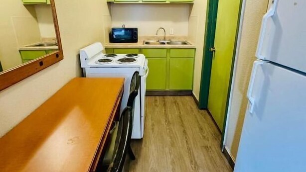 Una cocina compacta con gabinetes verdes, una estufa blanca y un refrigerador.