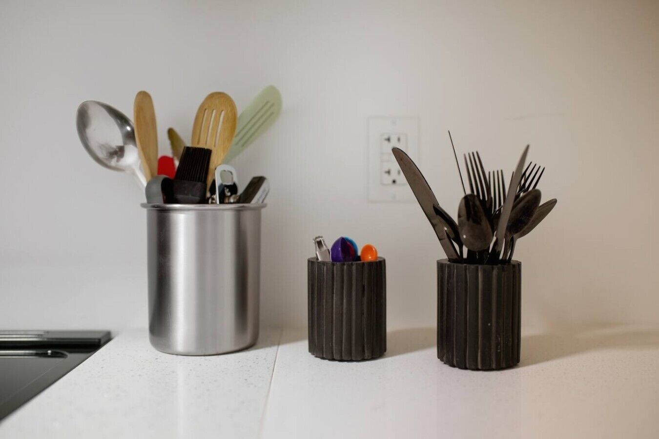Una encimera de cocina con tres soportes para utensilios que contienen diversas herramientas de cocina.