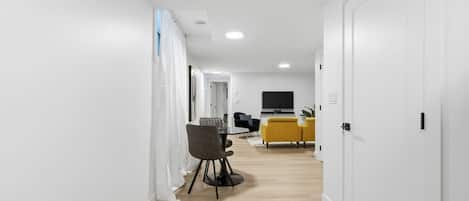 A hallway with a dining area, a TV, and a yellow sofa.