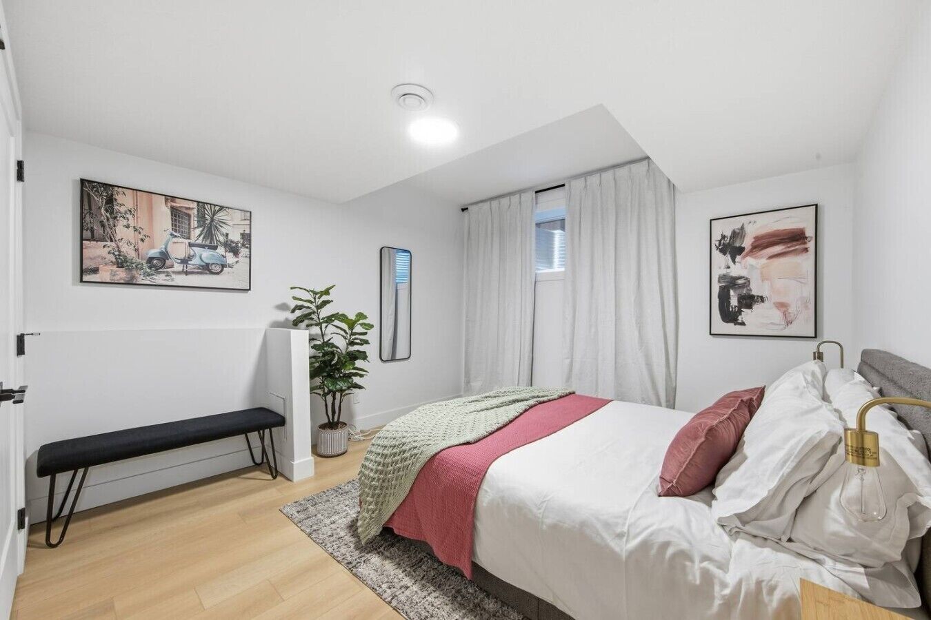 A bedroom with a bed, a bench, a potted plant, and artwork on the walls.