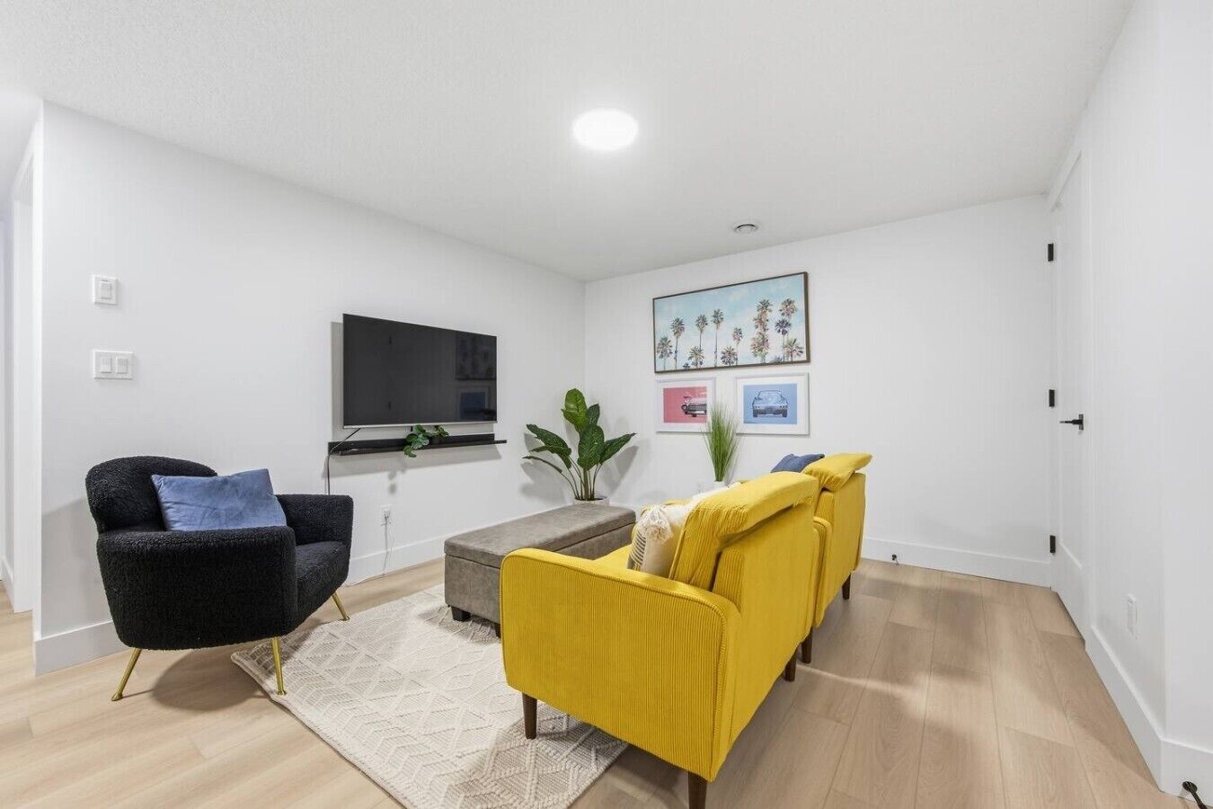 Ett modernt vardagsrum med en platt-TV, två soffor, ett soffbord och en krukväxt.
