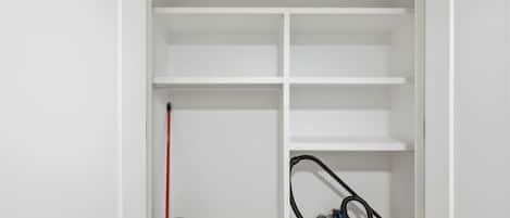 A white closet with multiple shelves and a vacuum cleaner on the floor.
