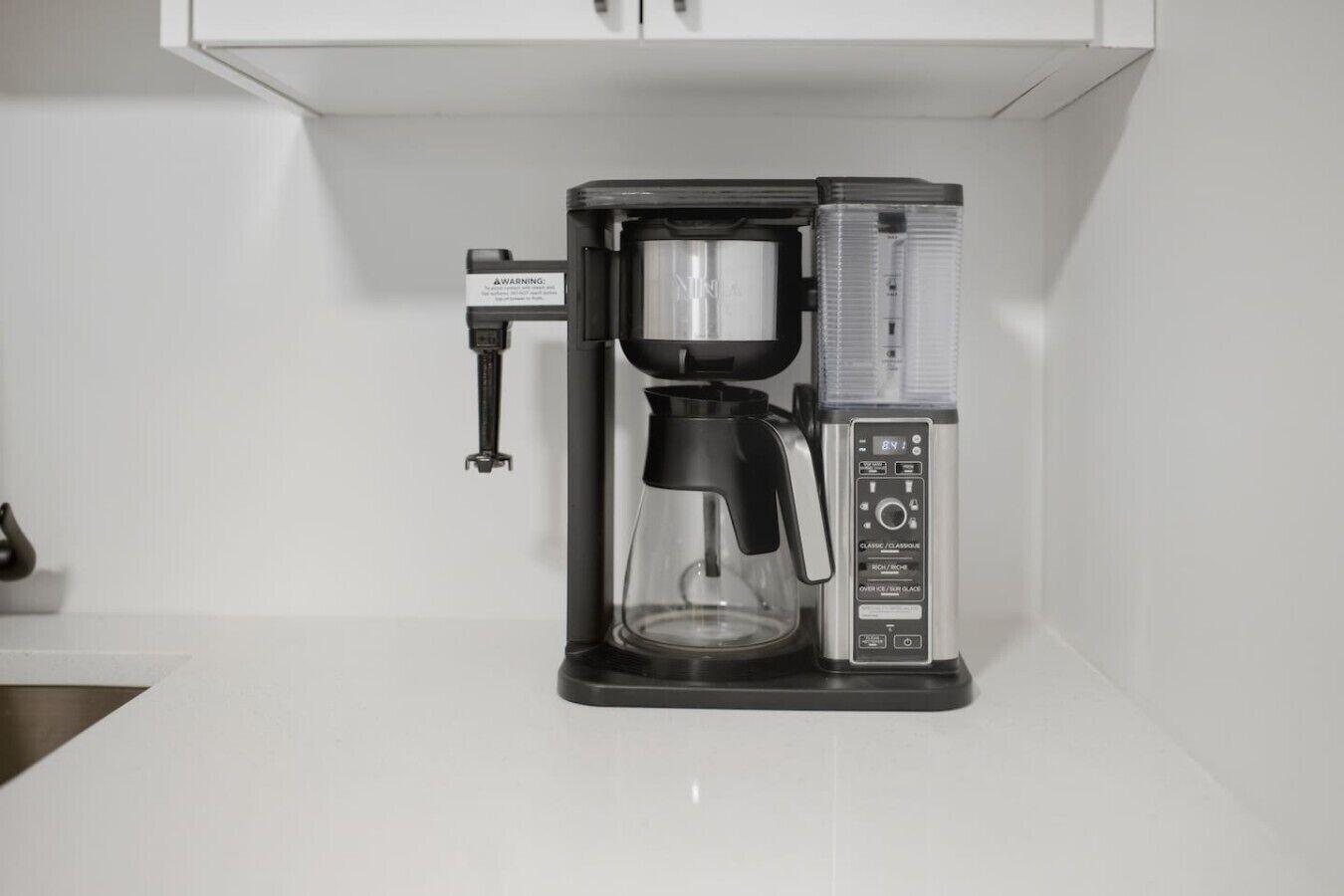 Une machine à café dotée d’un écran numérique et d’une verseuse, posée sur un plan de travail blanc.