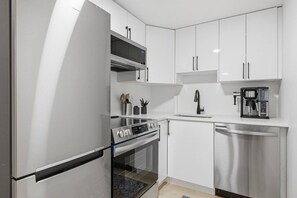 A modern kitchen with stainless steel appliances, white cabinetry, and a built-in oven. - The Pop Spot | 10 Min to Rogers | Blocks to 124St (Edmonton)