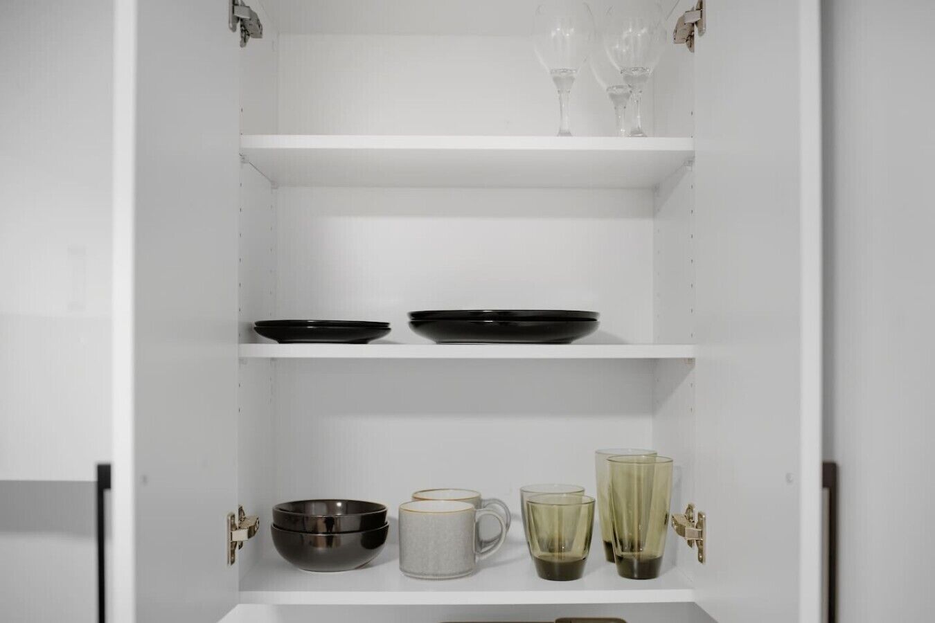 A white cabinet with shelves containing black plates, a white mug, and a glass pitcher.