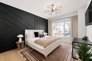 Ein modernes Schlafzimmer mit Bett, Nachttischen, Schreibtisch und großem Fenster.