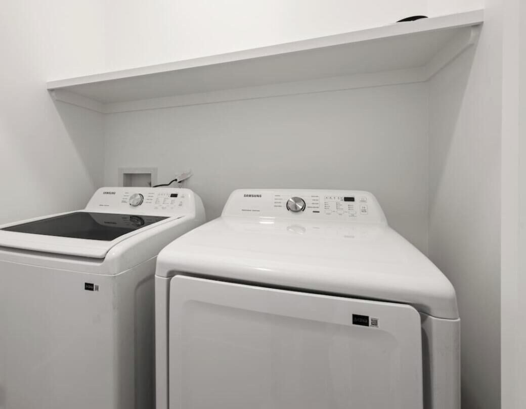 Deux machines à laver blanches, fixées au mur, se trouvent dans une buanderie dont le plafond et les murs sont également blancs.