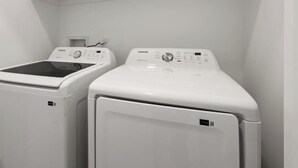 Två vita tvättmaskiner, monterade på väggen, i ett tvättrum med vita väggar och tak.