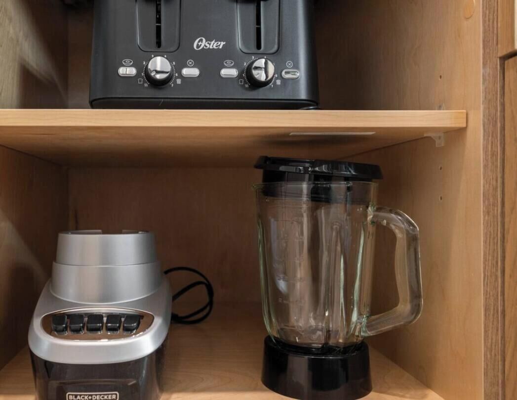 A kitchen with a toaster, a blender, and a wooden shelf.
