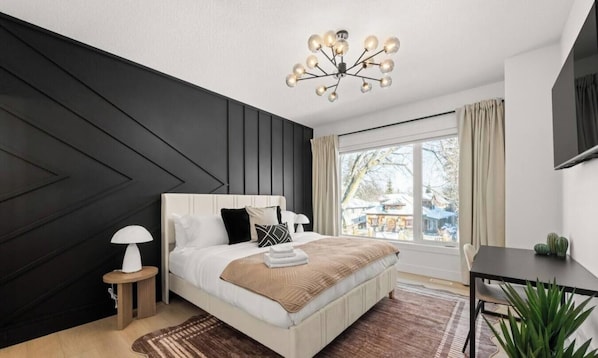 A modern bedroom with a large bed, bedside lamps, a view of the outdoors, and a dining area. - The Grande | AC |Garage | Yard | 10 min to Rogers (Edmonton)