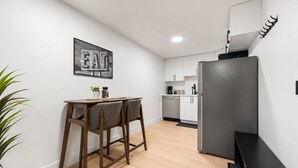 Una cocina moderna con comedor, armarios blancos, refrigerador negro y un letrero en la pared.